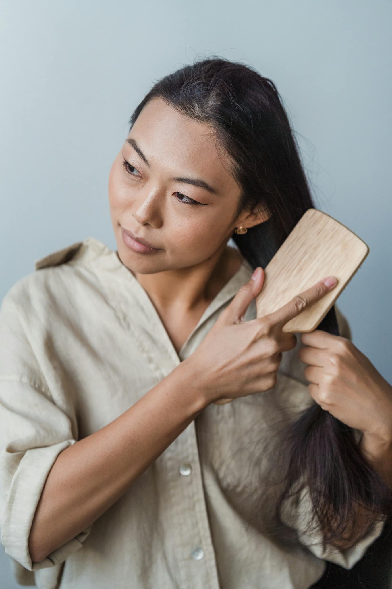 Asian woman brushing her long dark hair indoors as part of a beauty routine.