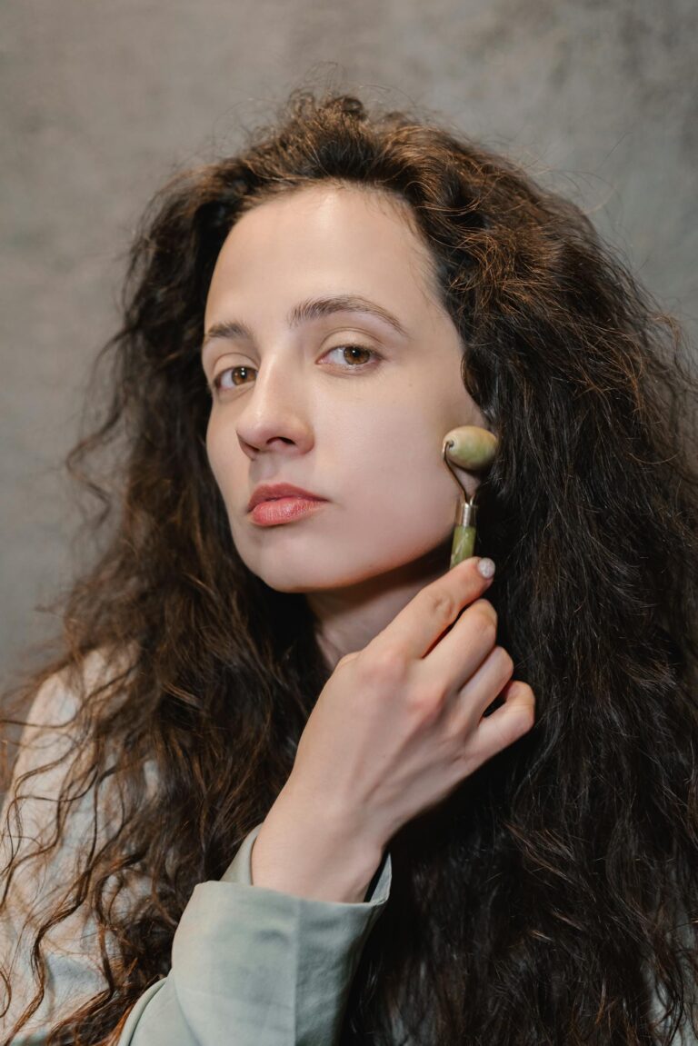 Portrait of a woman using a jade roller for a soothing skincare ritual indoors.